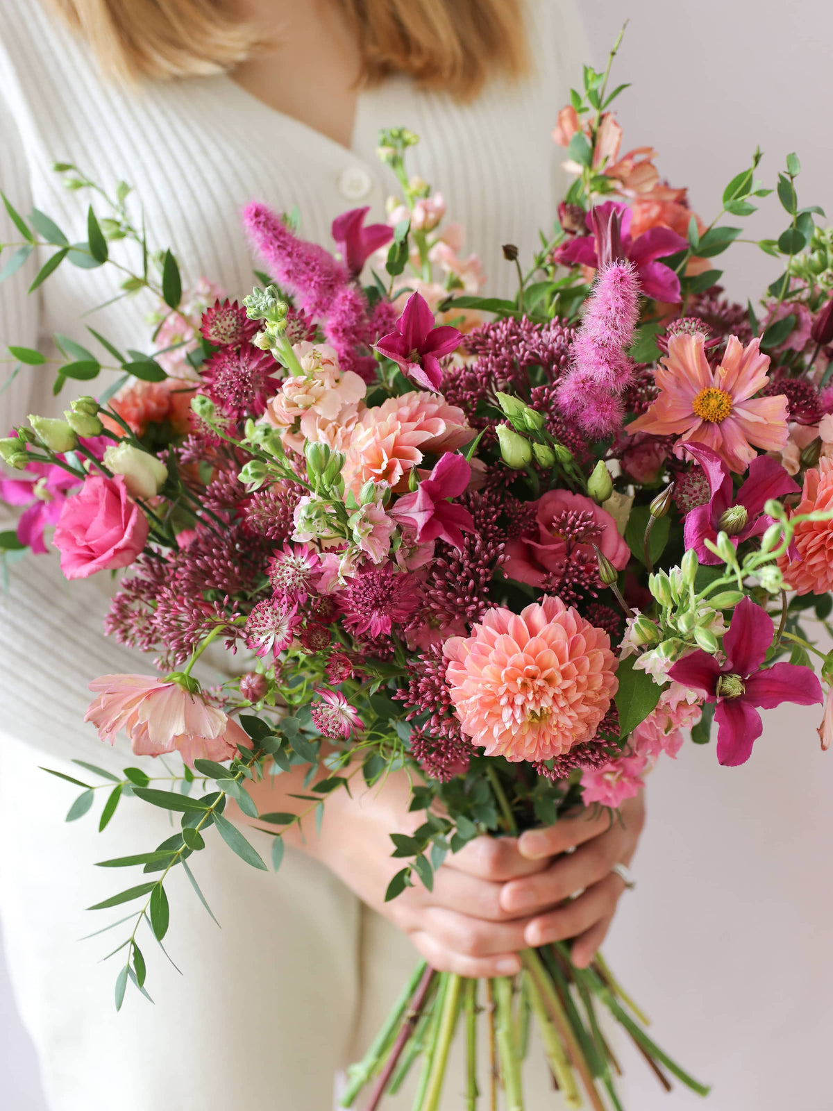 Bouquet of bright pink and peach flowers held by a person wearing a white sweater.