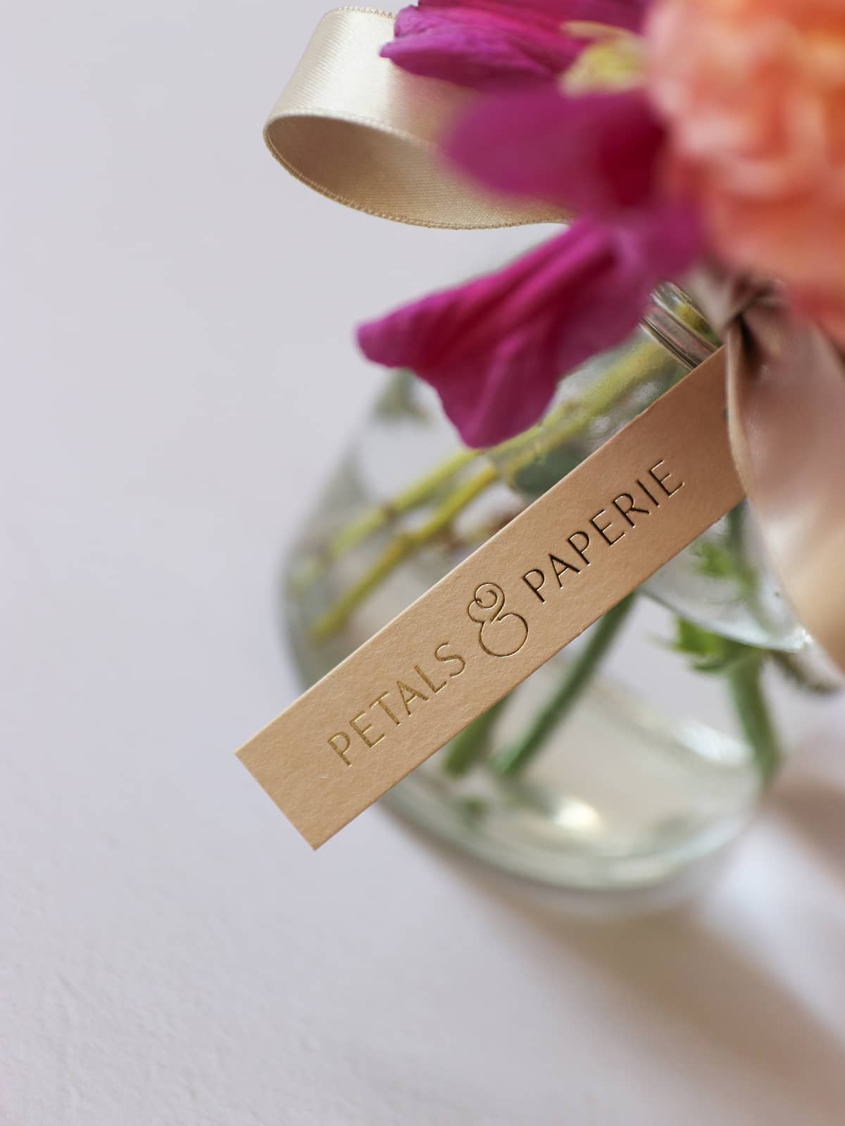 Glass vase with flowers and a 'Petals & Paperie' label on a light background