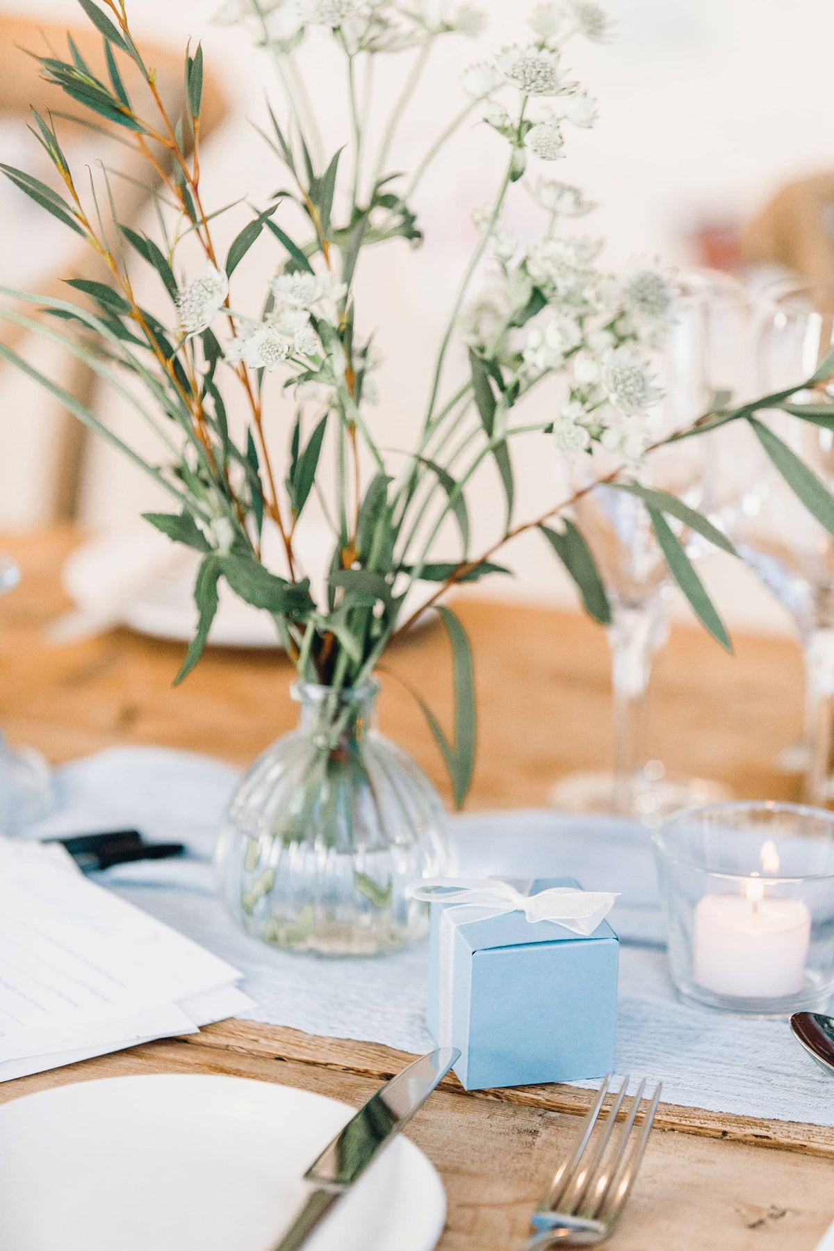 Decorative wedding table setting with pastel blue favour boxes and small bud vases containing white and blue flowers in a softly lit room at The Fig House, Middleton Lodge.