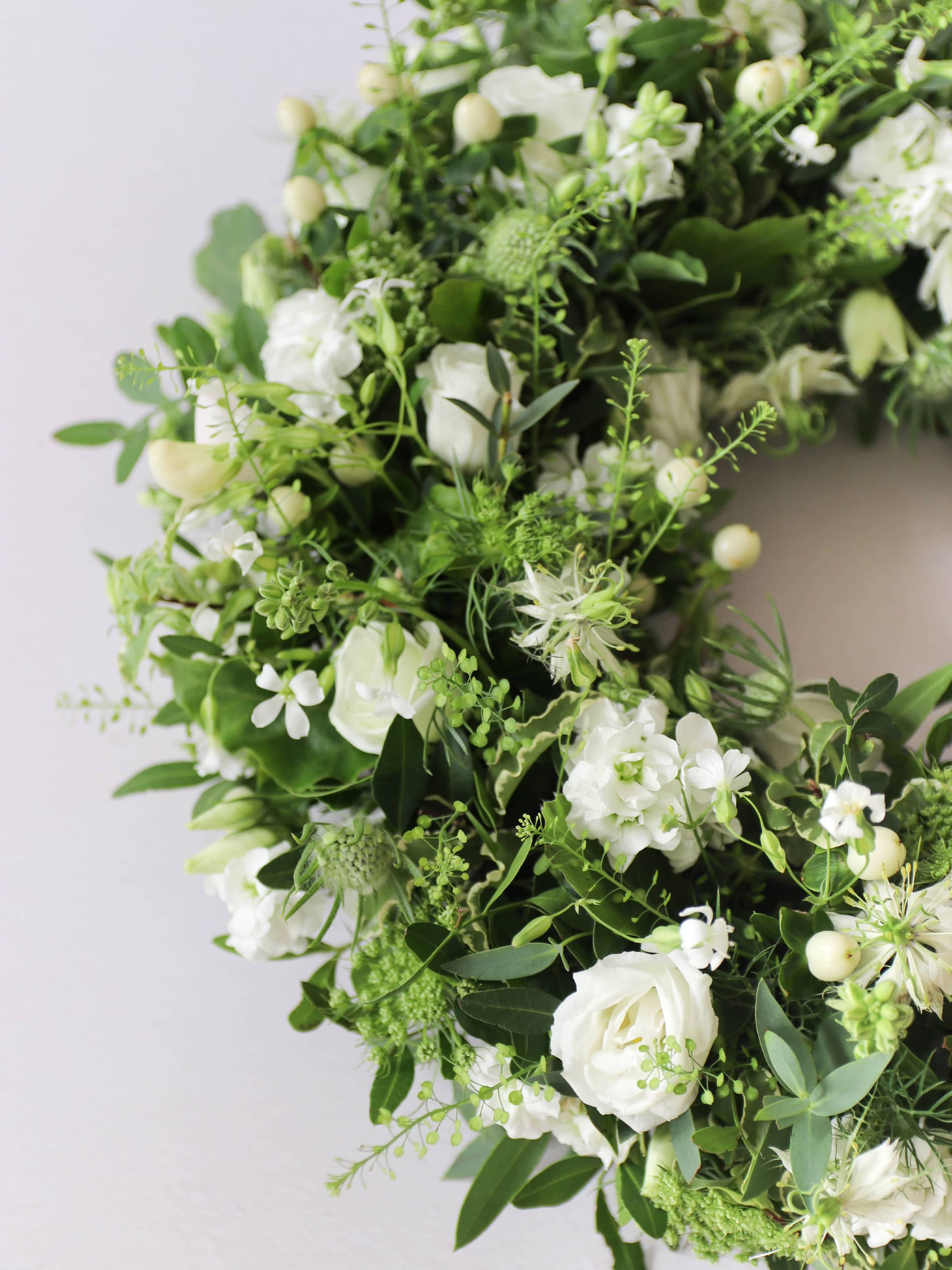 Close up of a funeral wreath with white and green flowers against a white background