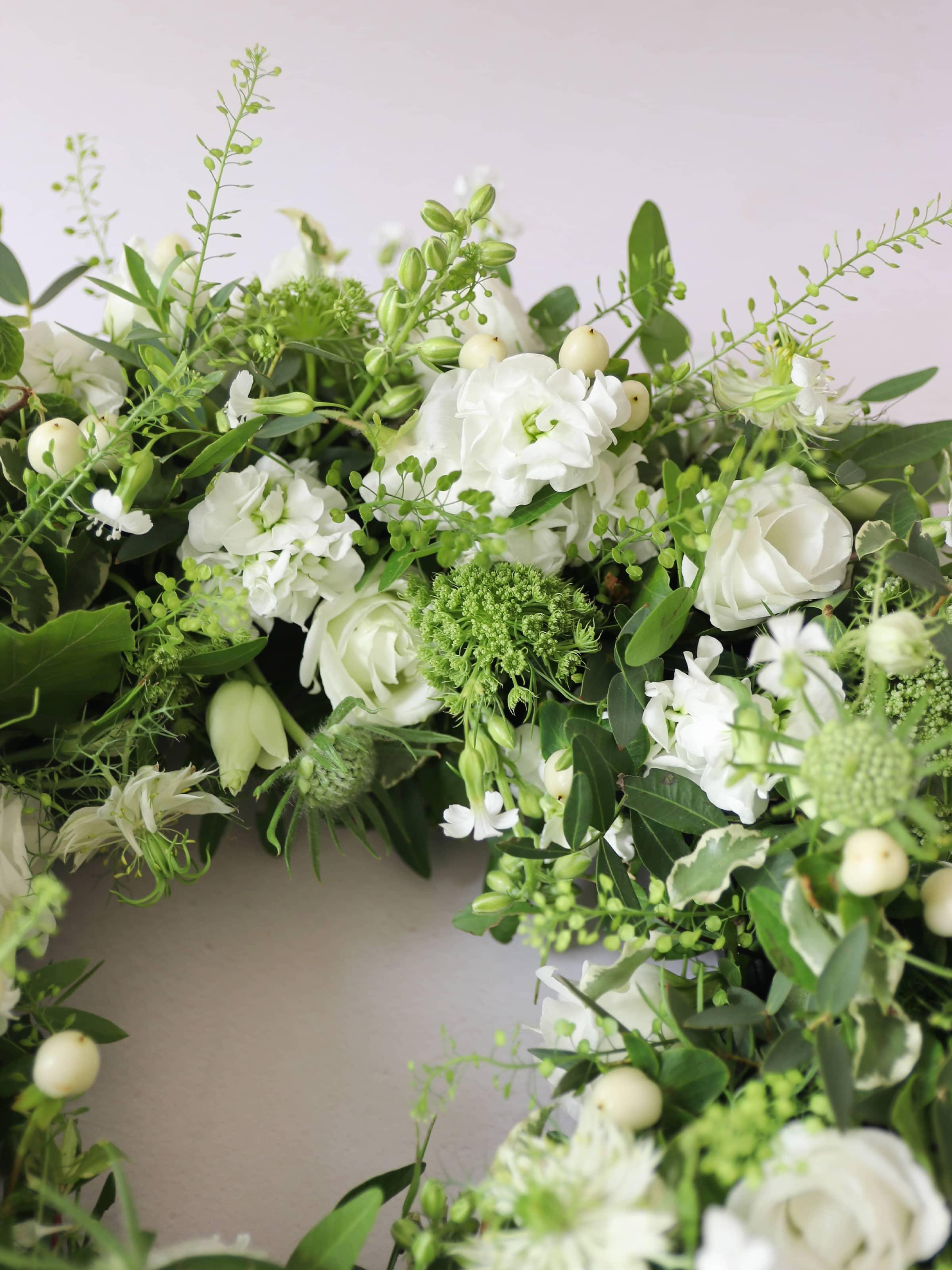 Close up of a funeral wreath with white and green flowers against a white background