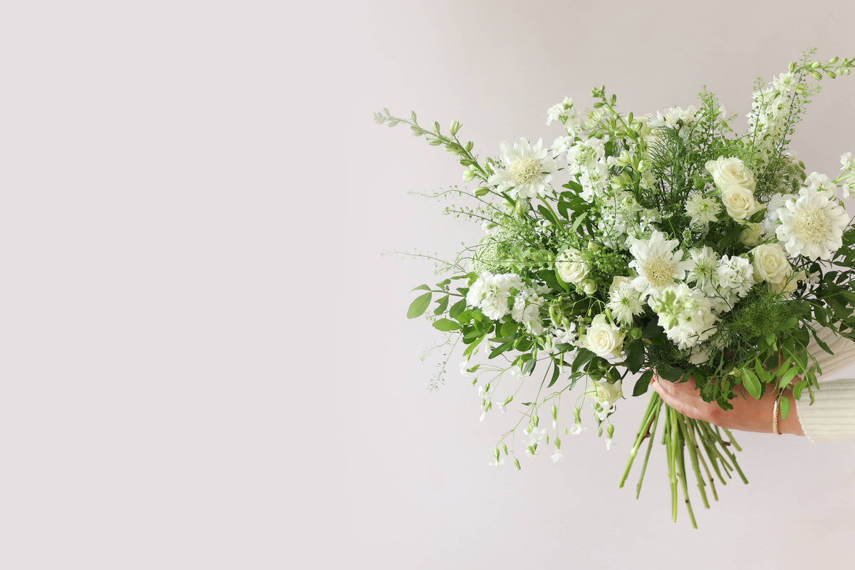 A bouquet of white and green flowers held out to the side by a person against a white background.