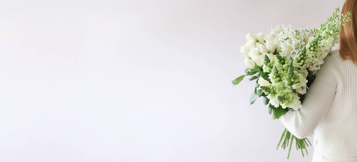 Bouquet of white and green flowers held by a woman on a light neutral background.