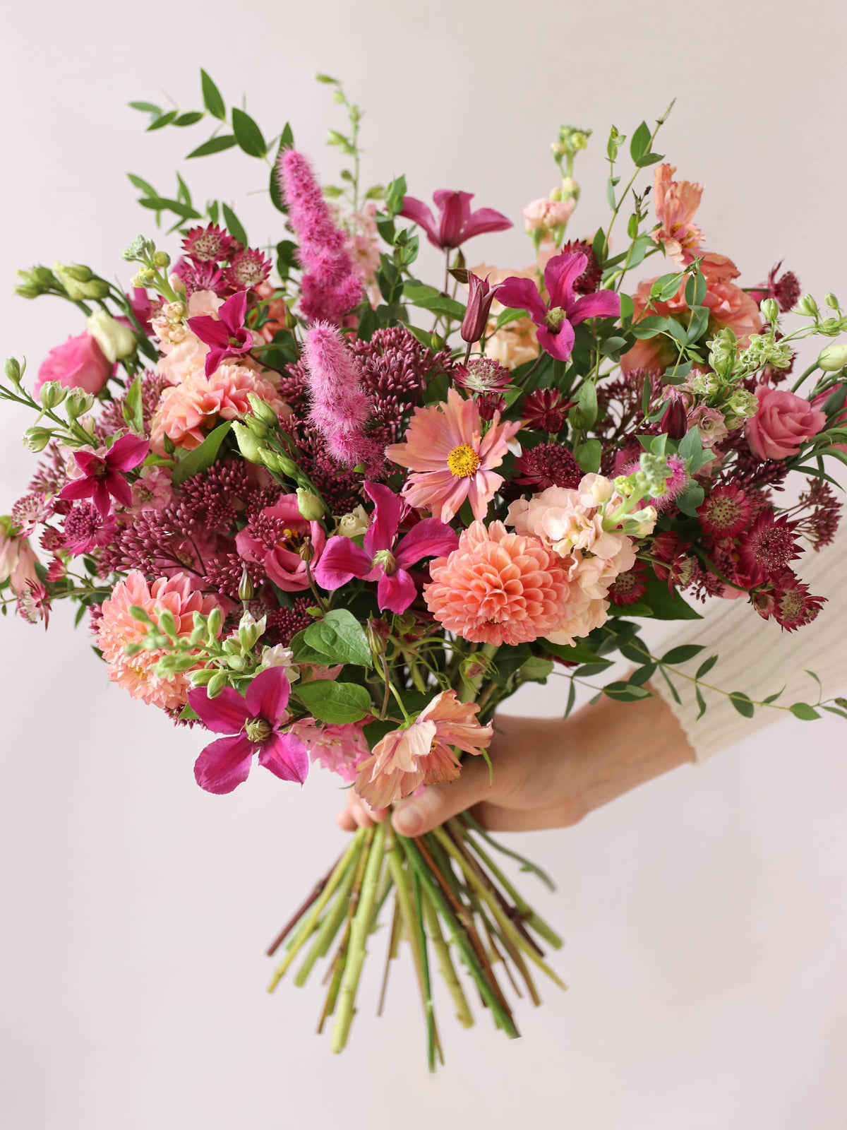 Bouquet of bright pink and peach flowers held by a hand against a light background