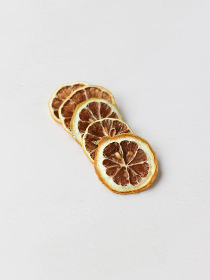 A top view of 5 dried lemon slices positioned in a diagonal row on a light neutral background.