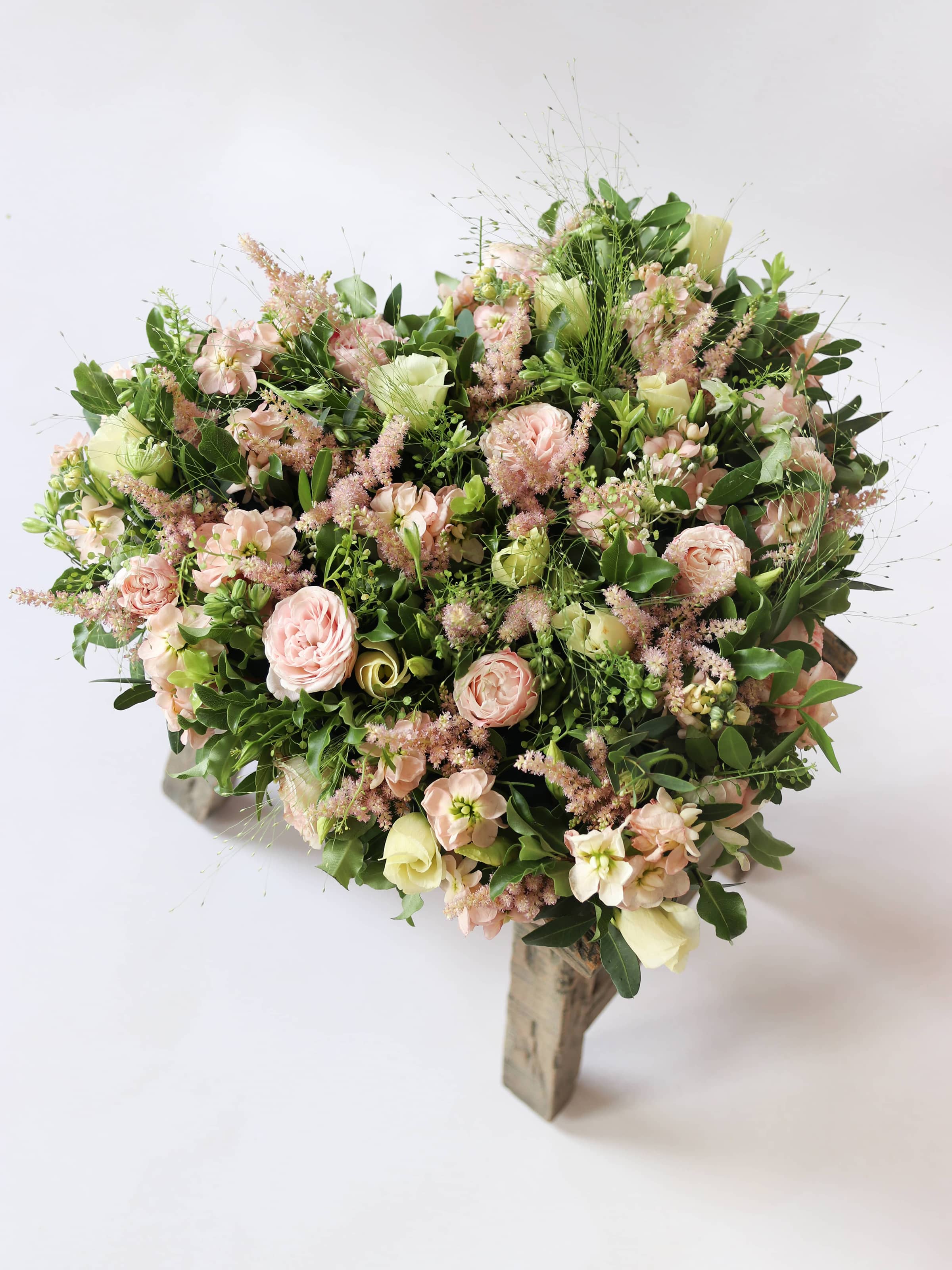 Heart shaped funeral posy with pink and green colours on a white background sitting on a wooden stool