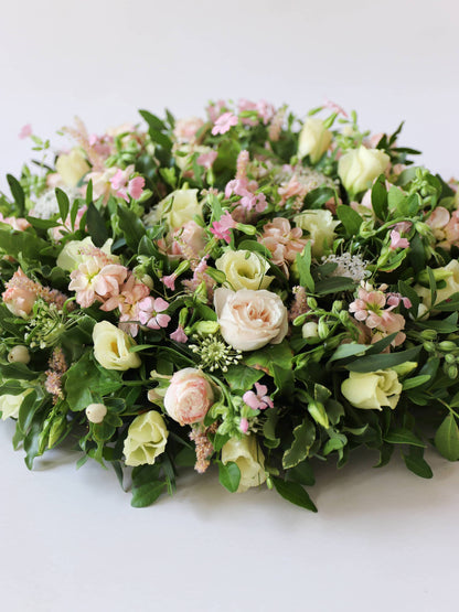Close up of a round funeral posy with white and pastel flowers on a white background