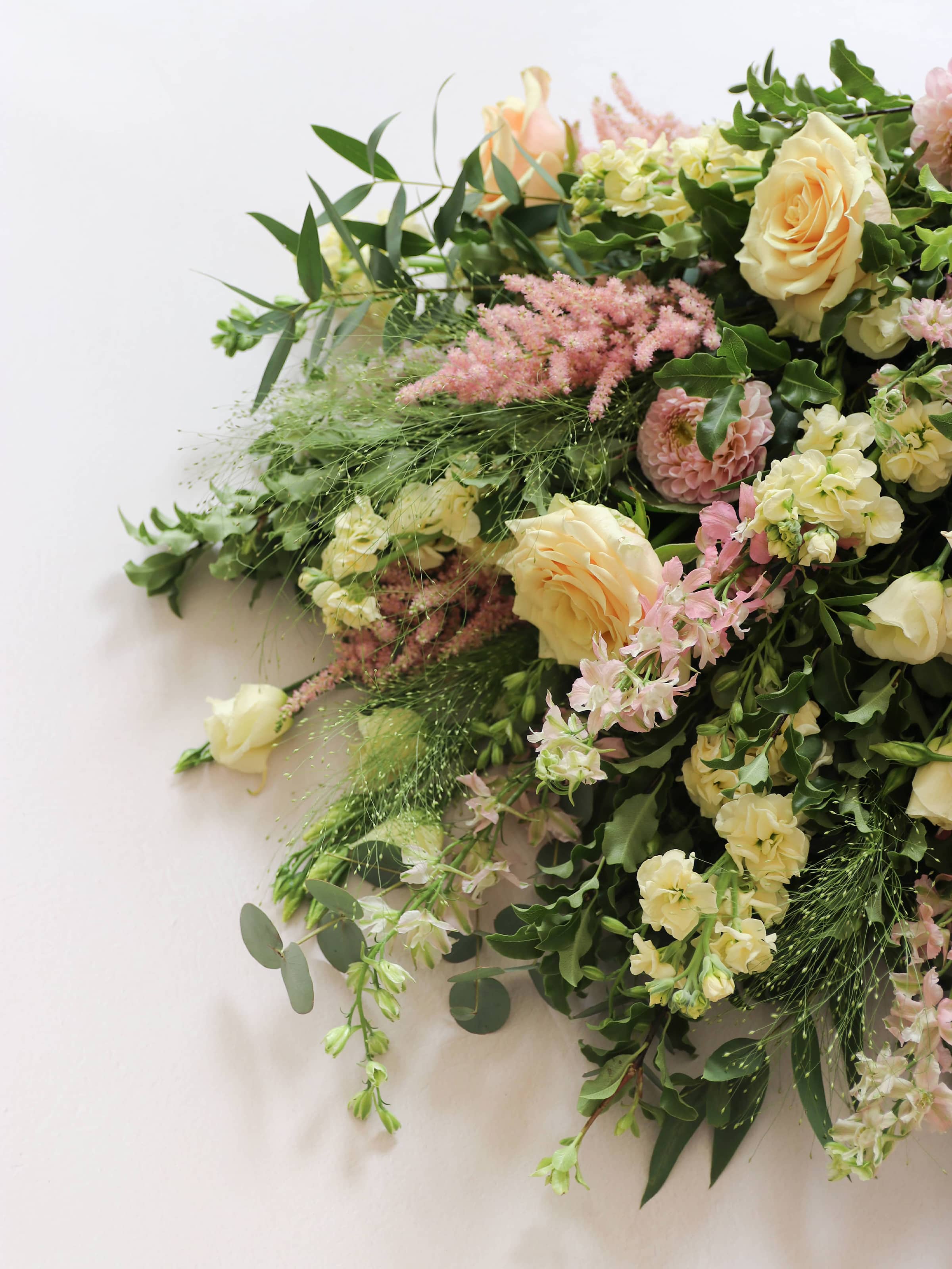 A detailed view of a pastel tied funeral sheaf containing pastel pink, peach and yellow flowers, tied with a satin pink ribbon.