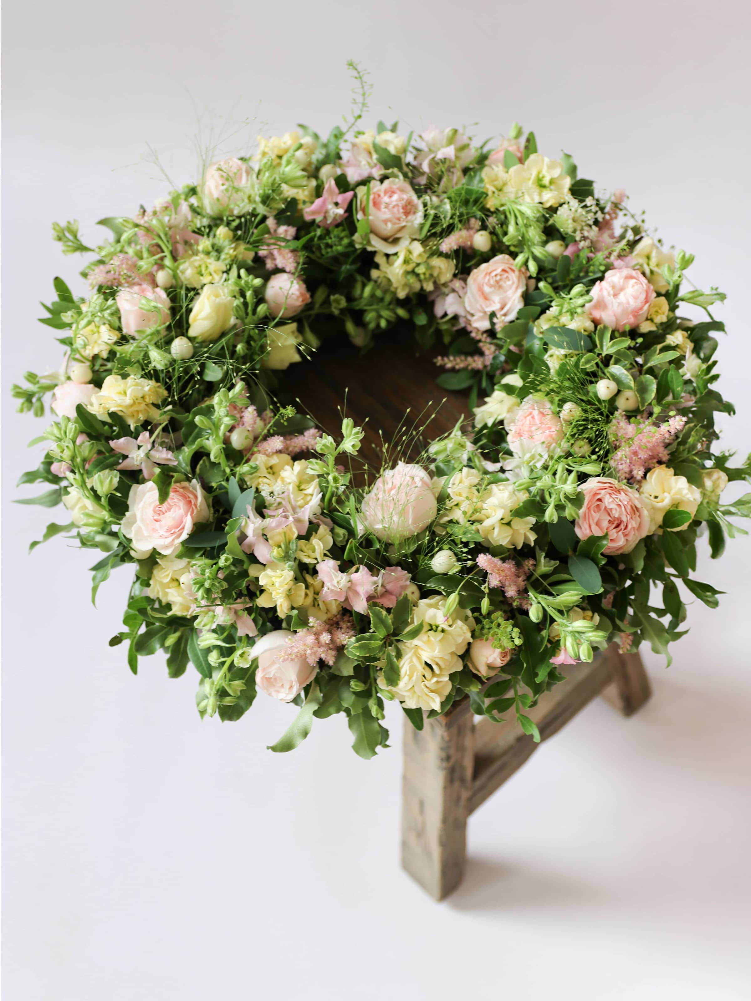 Funeral wreath with pastel and green flowers on a wooden stool against a white background