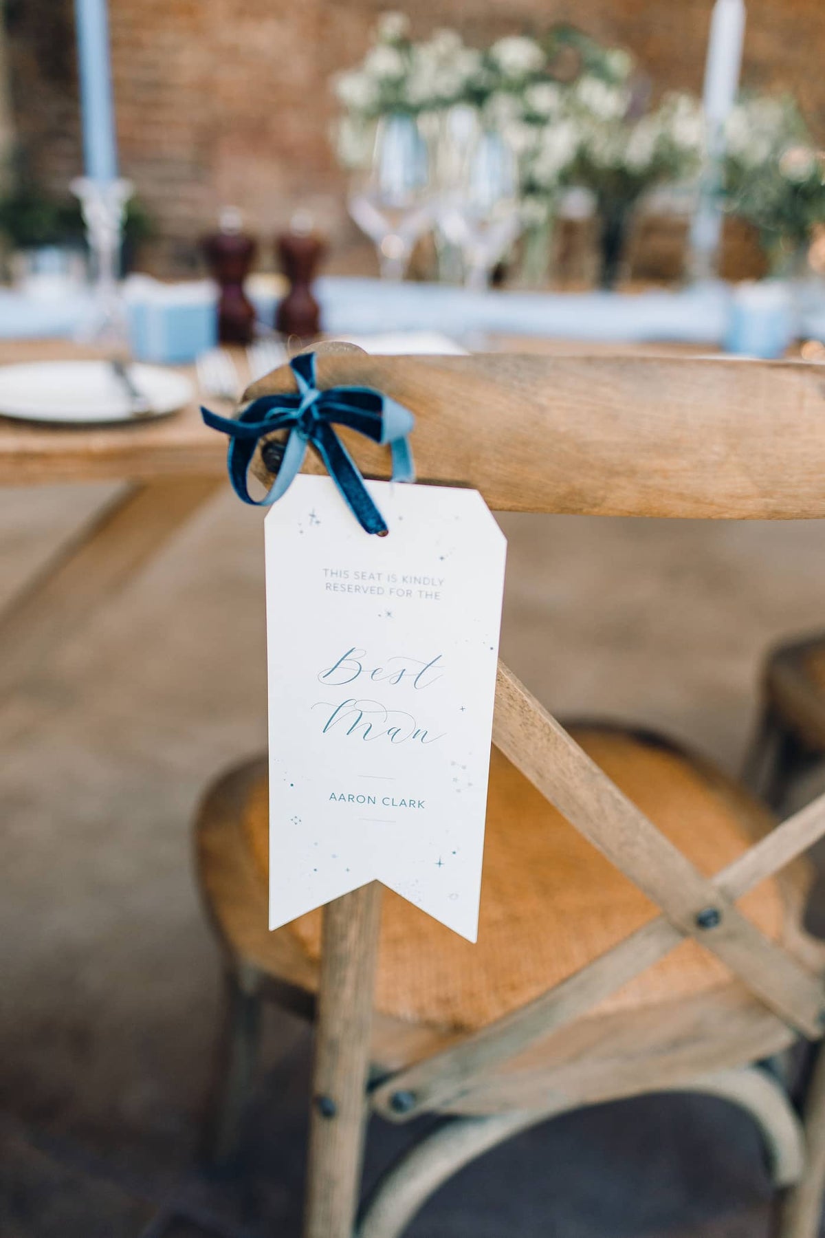 A rustic wooden chair at a wedding reception with a 'Best Man' tag, tied with a blue velvet ribbon.