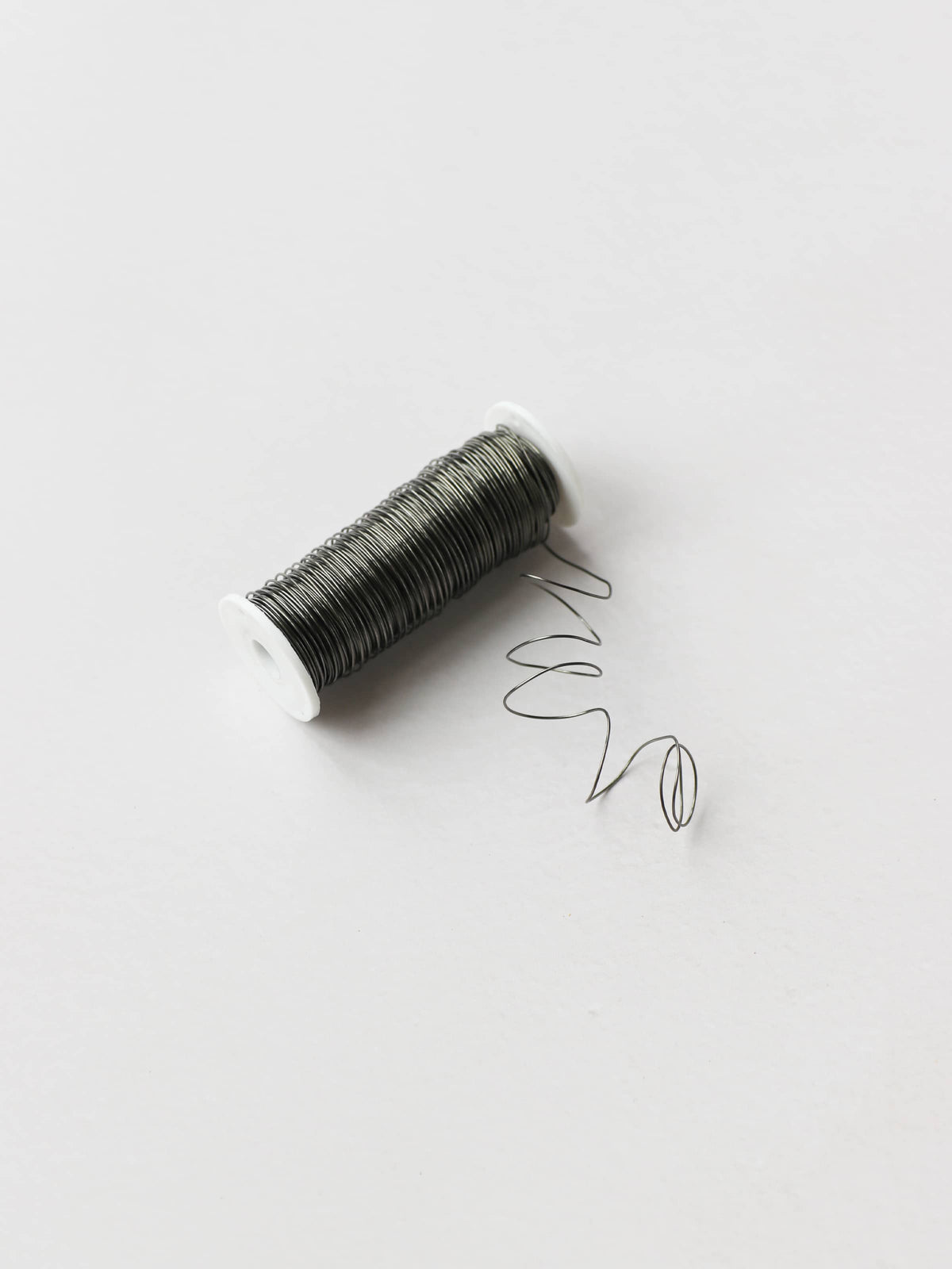 A spool of silver reel wire for Christmas wreath making, on a neutral background.