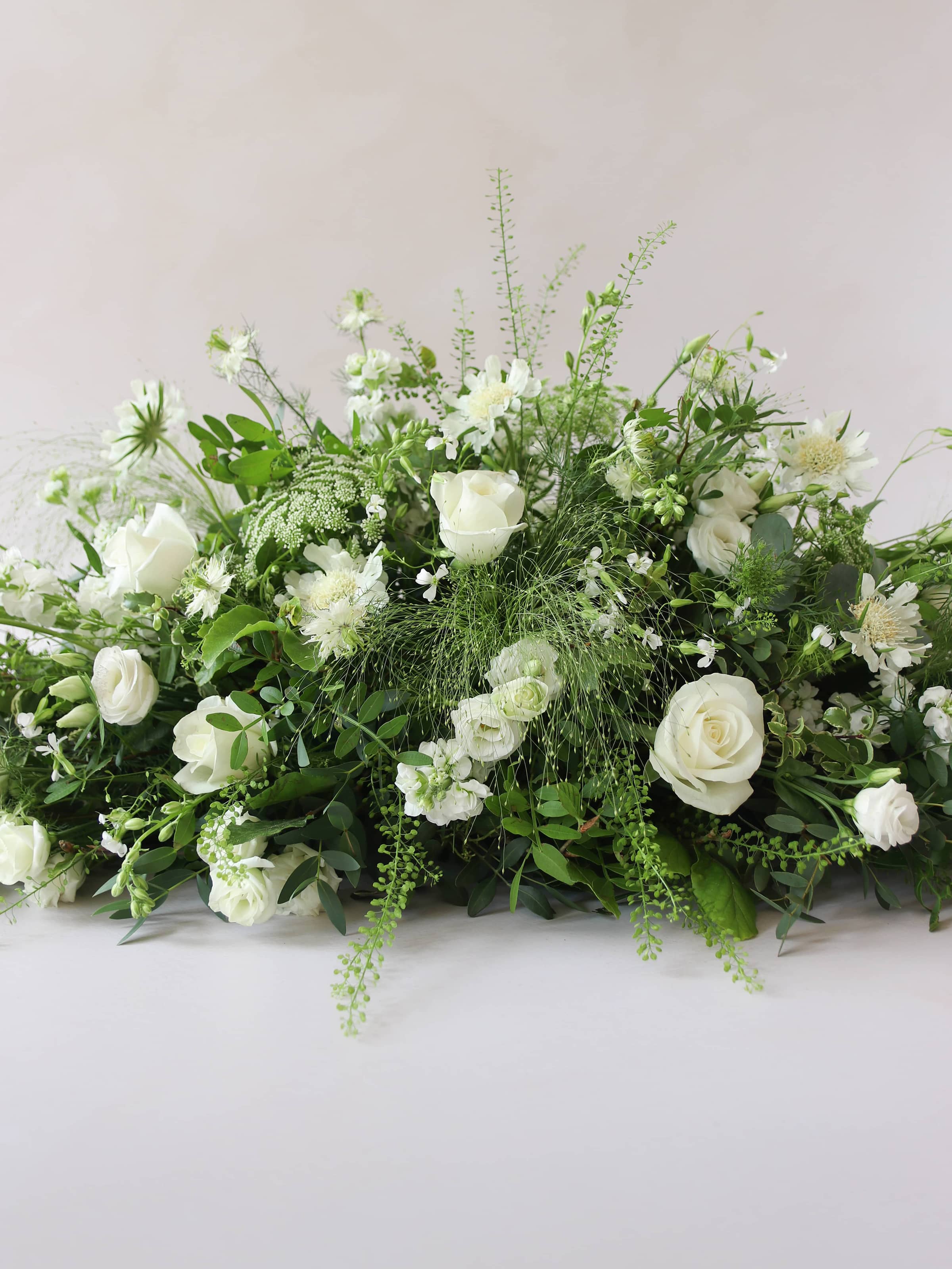 A close up of the middle section of a 3ft coffin spray featuring white and green flowers and foliage. The funeral arrangement is sitting against a neutral background and features white Roses, Ammi, Stocks and Lisianthus. 